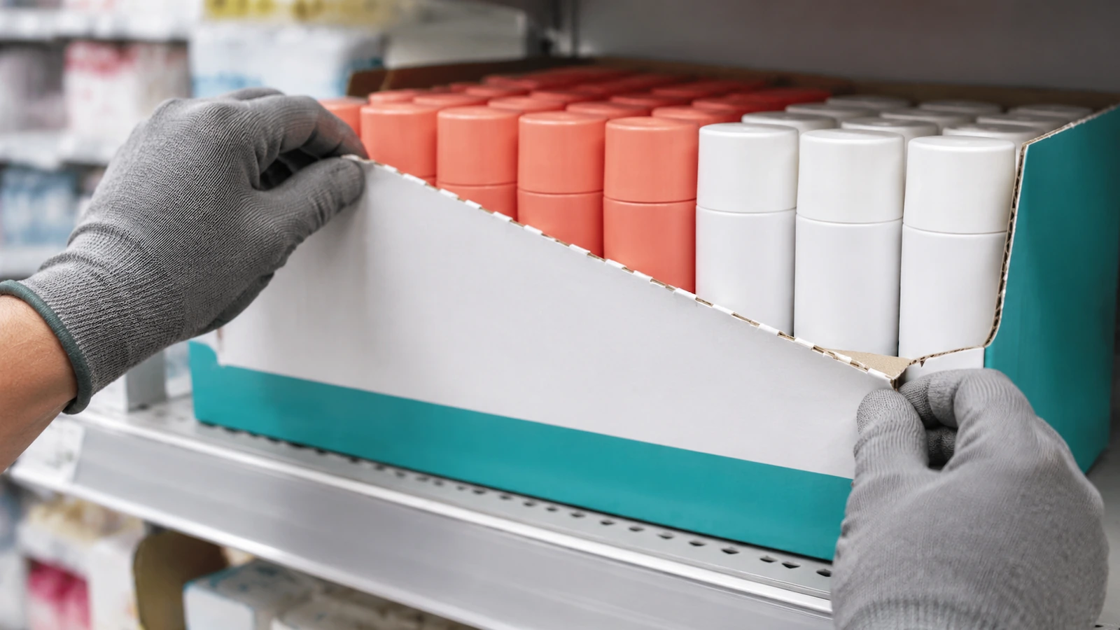 Mains retirant le panneau avant perforé d'un plateau prêt pour le rayon en carton ondulé, qui laisse apparaître des produits soigneusement rangés, prêts pour le rayon