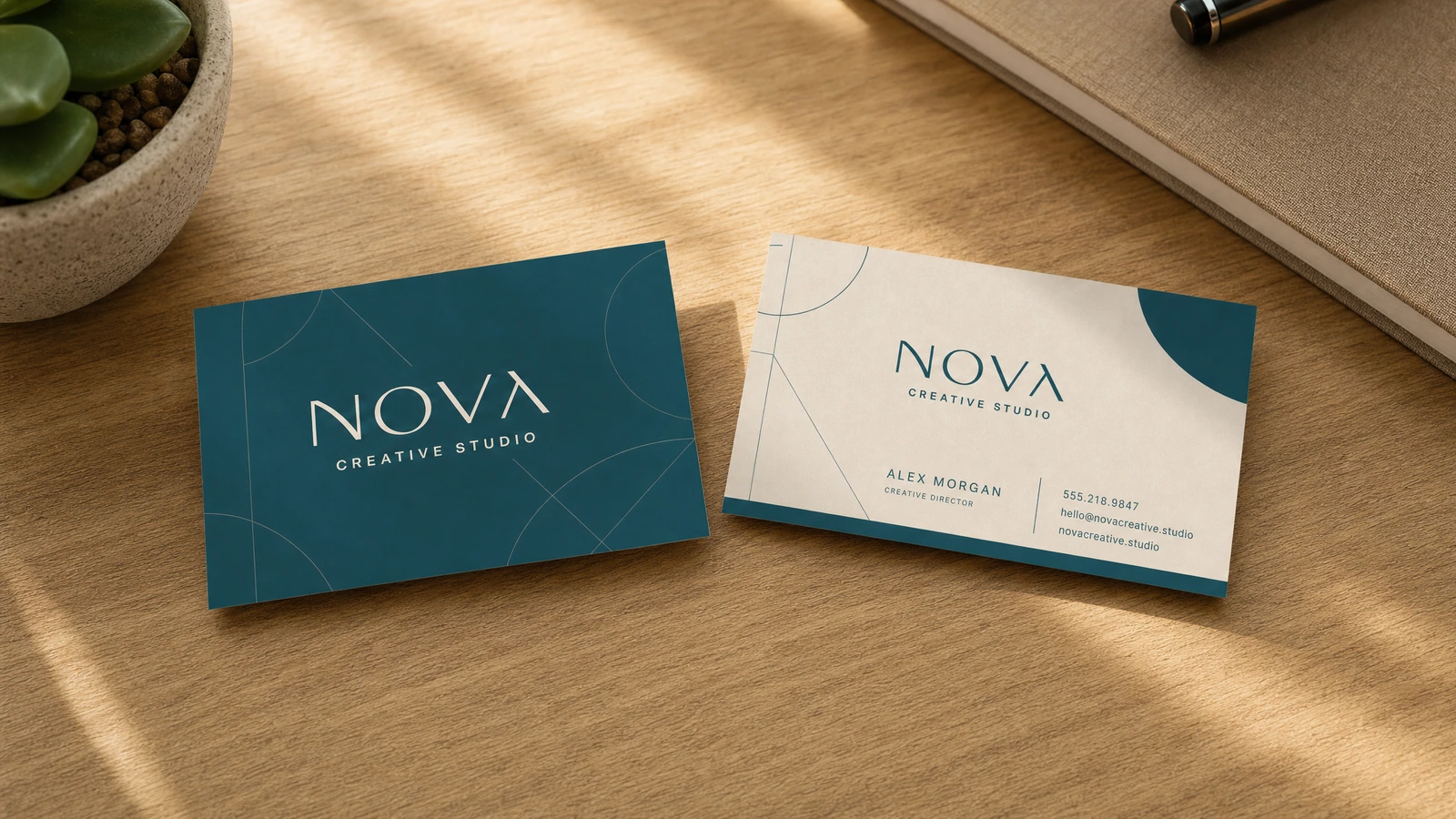 Cartes de visite illustratives turquoise et crème sur un bureau en bois, à côté d'un carnet