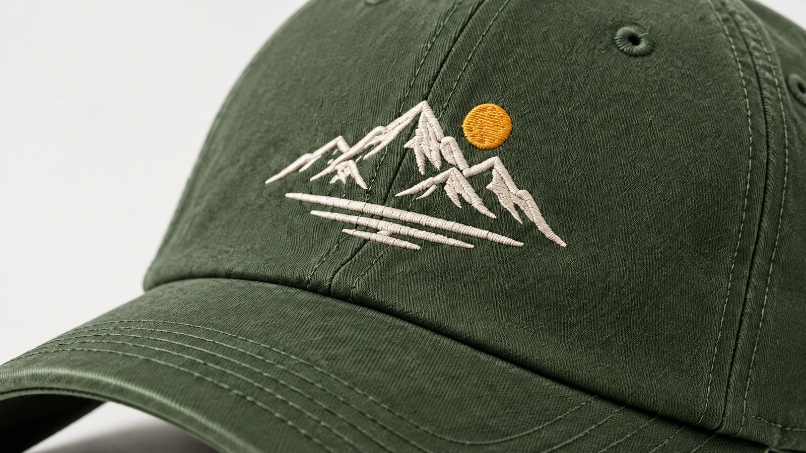 Gros plan d'une broderie de montagne blanche et d'un soleil jaune sur une casquette verte