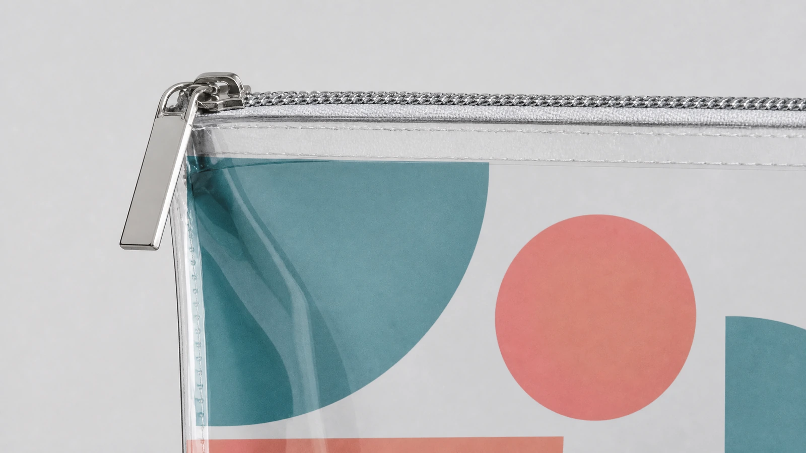 Gros plan sur un curseur de fermeture éclair argenté et sur un coin de pochette transparente imprimée