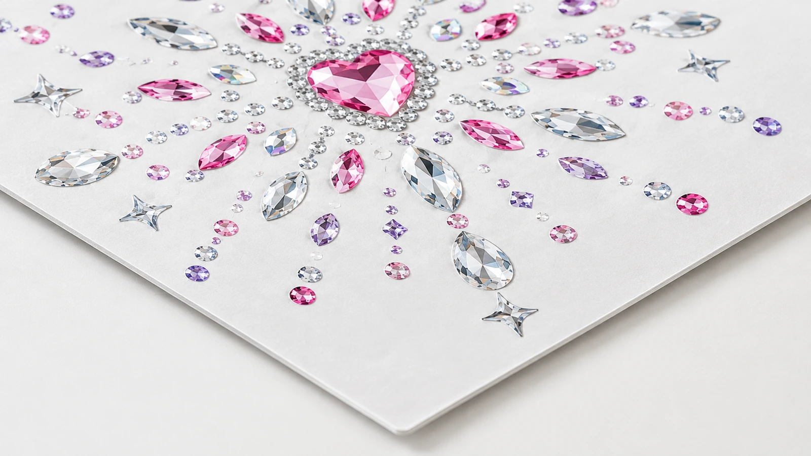 Gros plan d'un motif en strass rose à centre en forme de cœur, avec des pierres transparentes, roses et violettes, sur une feuille blanche