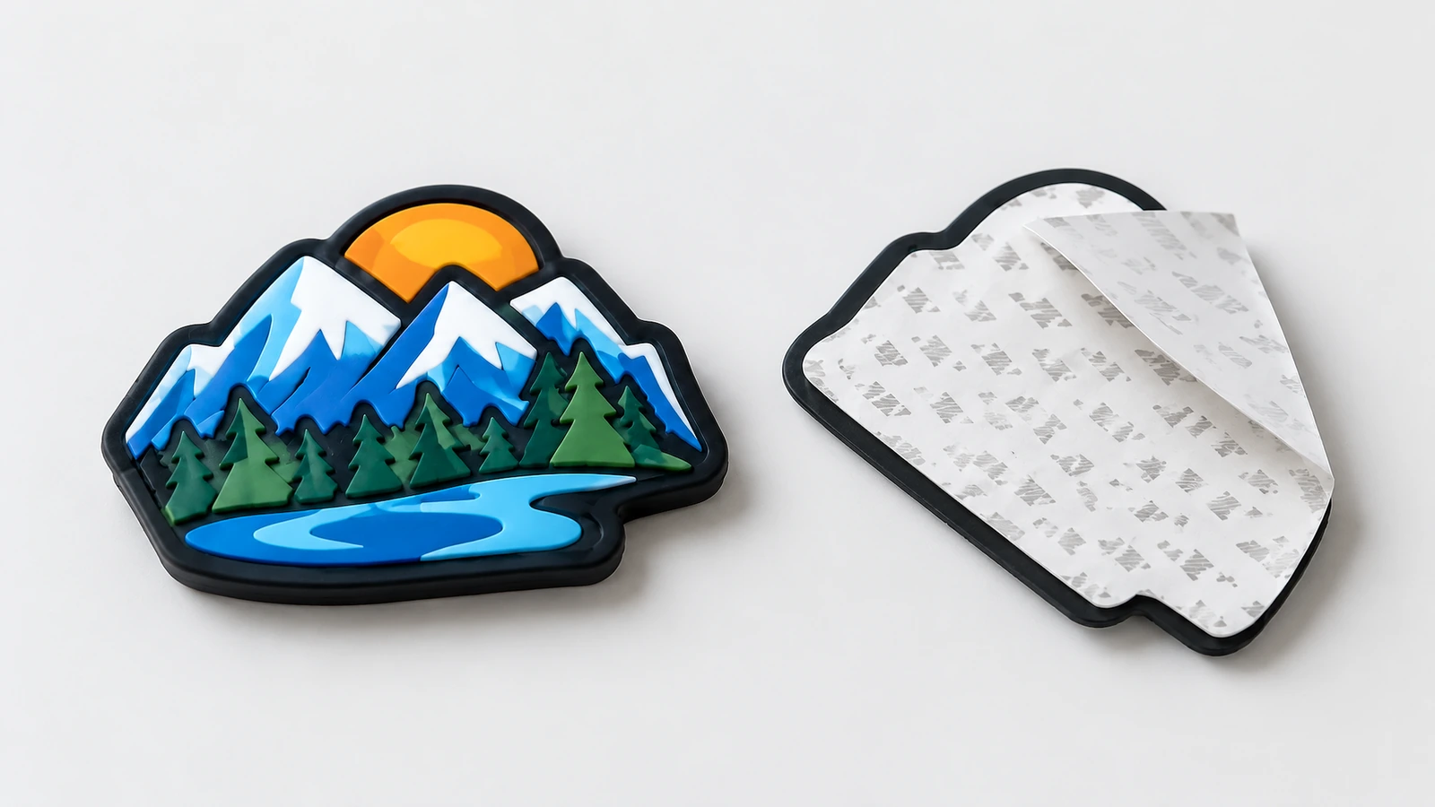 Étiquette PVC souple au design montagne vue de face, à côté de son support adhésif et de son film de protection partiellement décollé