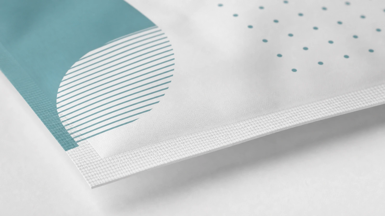 Détail de l'impression et du bord scellé du sachet Gros plan sur l'impression géométrique bleu sarcelle et le bord scellé texturé d'un sachet blanc
